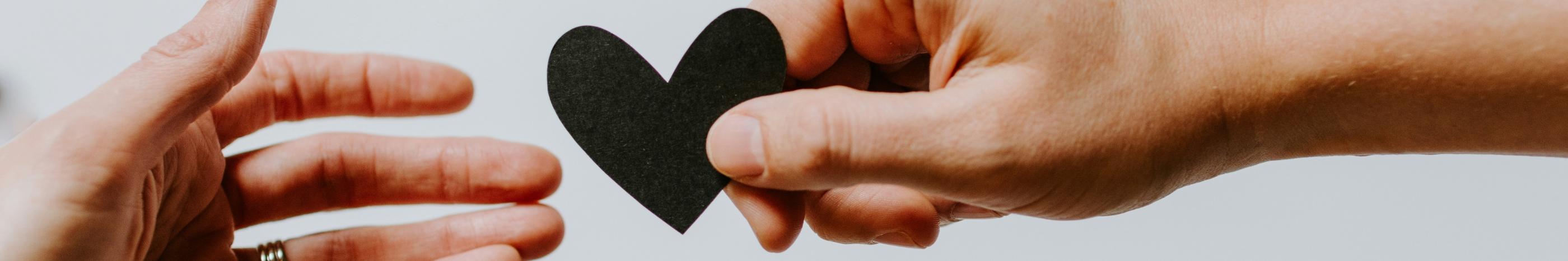 Zwei Hände reichen sich ein ausgeschnittenes Papierherz