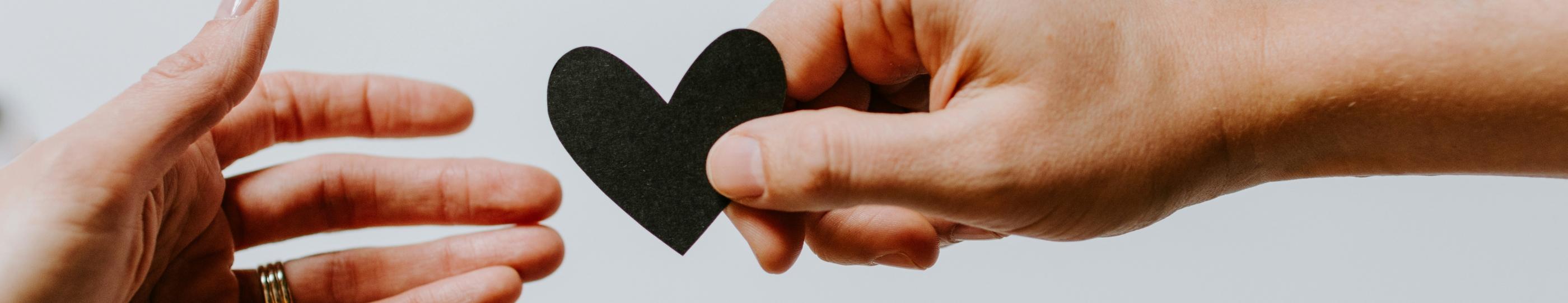 Zwei Hände reichen sich ein ausgeschnittenes Papierherz